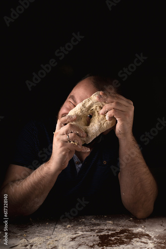 A man looks through a hole in the dough against a dark background. Pizza dough preparation.