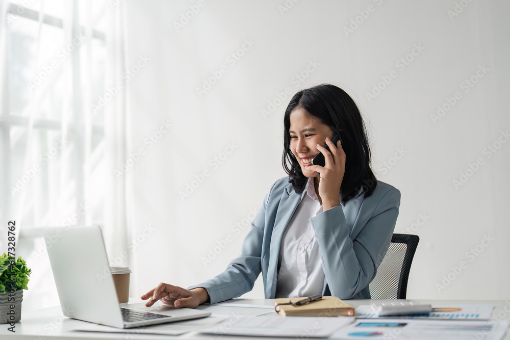 Attractive young business woman talking on the mobile phone and smiling while sitting at her working place in office and at laptop Attractive young business woman talking on the mobile phone and smiling while sitting at her working place in office and at laptop