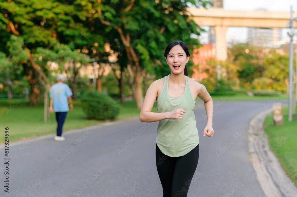 Fit Asian young woman jogging in park smiling happy running and enjoying a healthy outdoor lifestyle. Female jogger. Fitness runner girl in public park. healthy lifestyle and wellness being concept Fit Asian young woman jogging in park smiling happy running and enjoying a healthy outdoor lifestyle. Female jogger. Fitness runner girl in public park. healthy lifestyle and wellness being concept
