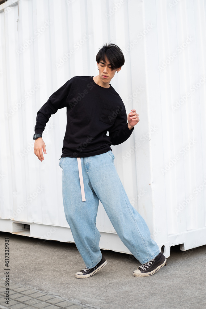 Portrait of stylish handsome asian model wearing black casual hoodie and jeans, posing near the wall on the street, urban lifestyle Portrait of stylish handsome asian model wearing black casual hoodie and jeans, posing near the wall on the street, urban lifestyle