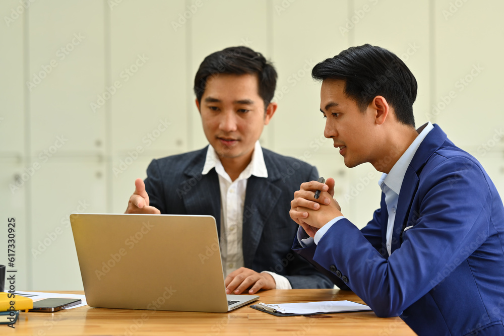 Shot of two startup businessman using laptop and discussing company financial project together Shot of two startup businessman using laptop and discussing company financial project together