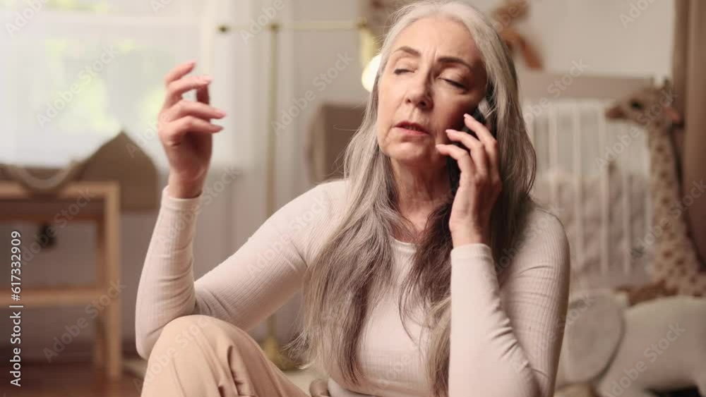 Serious gray haired senior woman talking by smartphone with family or friends share news at light cozy home Confident mature female having conversation on mobile phone device gadget indoors Serious gray haired senior woman talking by smartphone with family or friends share news at light cozy home Confident mature female having conversation on mobile phone device gadget indoors