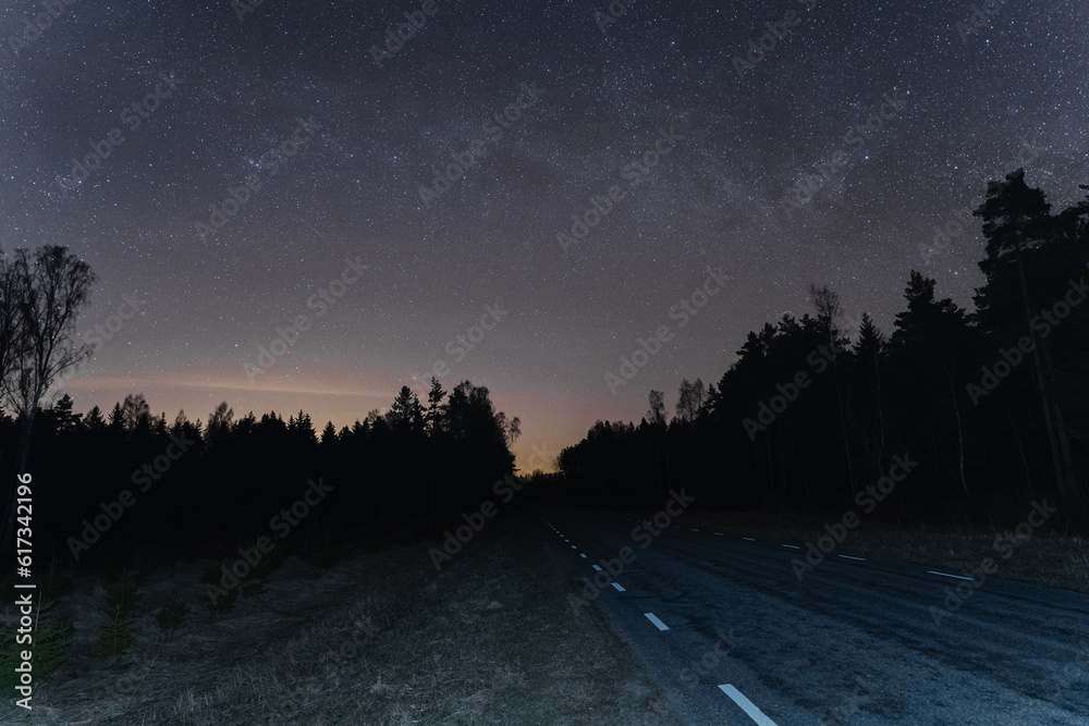 Road at night through the forest, starry sky in autumn in Estonia.