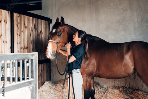 Fotografie young female groom in the stable takes care of her stallion