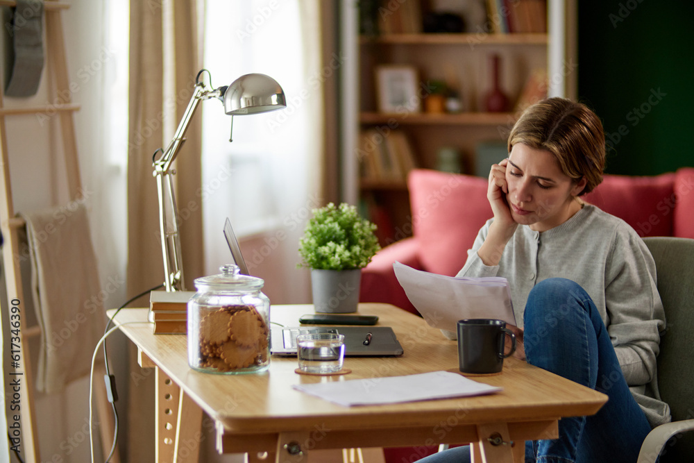 Mid adult woman examining her bank statement at home office Mid adult woman examining her bank statement at home office