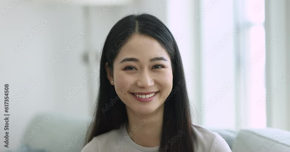 Head shot close up of happy beautiful single Asian young woman smile look at camera seated on couch at home, video call participant profile picture, relaxation at own or rented flat. Tenant portrait Head shot close up of happy beautiful single Asian young woman smile look at camera seated on couch at home, video call participant profile picture, relaxation at own or rented flat. Tenant portrait