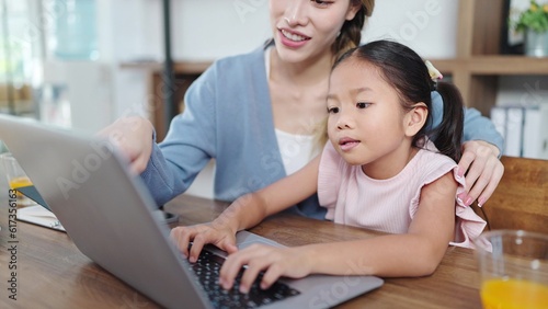 Happy asian mother and little daughter using laptop for studying online or doing homework. Mother helping daughter using laptop. Online education, Technology concept