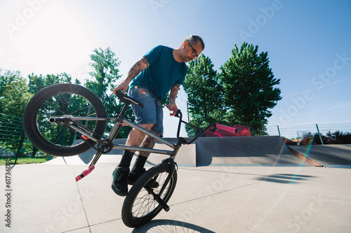 An urban oldish guy is doing a 360 rotation trick on his bmx in a skate park.