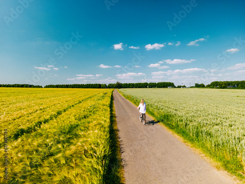 Aerial drone shot of young woman cyclist riding down beautiful countryside road between agricultural fields on sunny summer day. Healthy lifestyle © nikkimeel