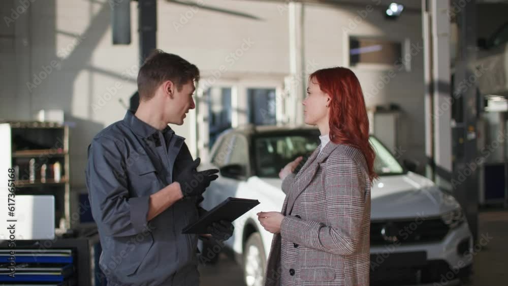 automobile maintenance, male mechanic uses modern technology and shows technical moment of car on tablet beautiful female client, smiles and looks at camera automobile maintenance, male mechanic uses modern technology and shows technical moment of car on tablet beautiful female client, smiles and looks at camera