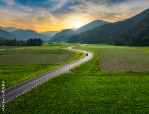 Wallpaper Mural Top drone view of beautiful landscape with alpine mountains, paved highway, hills, fields green grass. Aerial view of beautiful curved rural road in green meadows at sunset in summer in Slovenia Torontodigital.ca