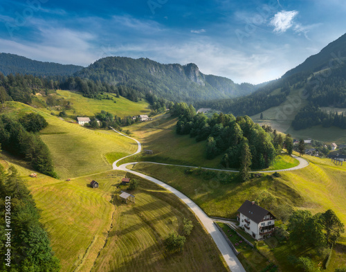 Aerial view of long winding country road leading through green hills at sunset in summer. Colorful landscape with curved rural road in green meadows. Alpine mountains, blue sky with clouds. Slovenia © kucherav