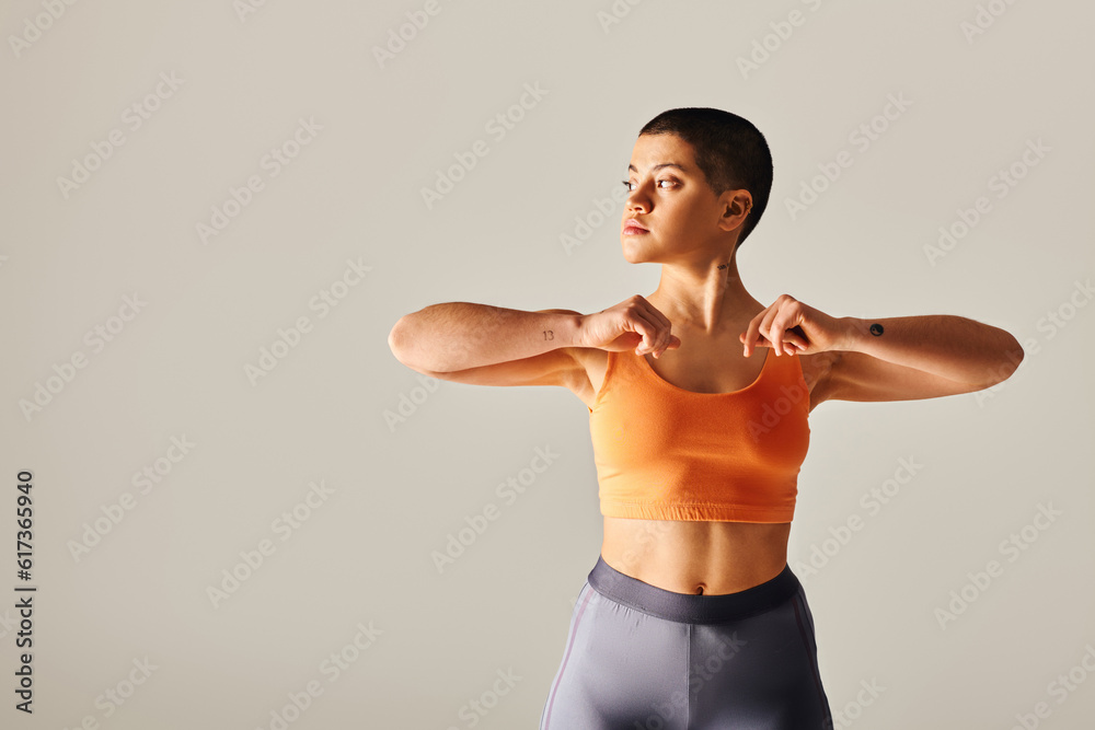 body diversity, tattooed and short haired woman exercising and looking away on grey background, curvy fitness model in sportswear, empowerment, motivation, strength and health body diversity, tattooed and short haired woman exercising and looking away on grey background, curvy fitness model in sportswear, empowerment, motivation, strength and health
