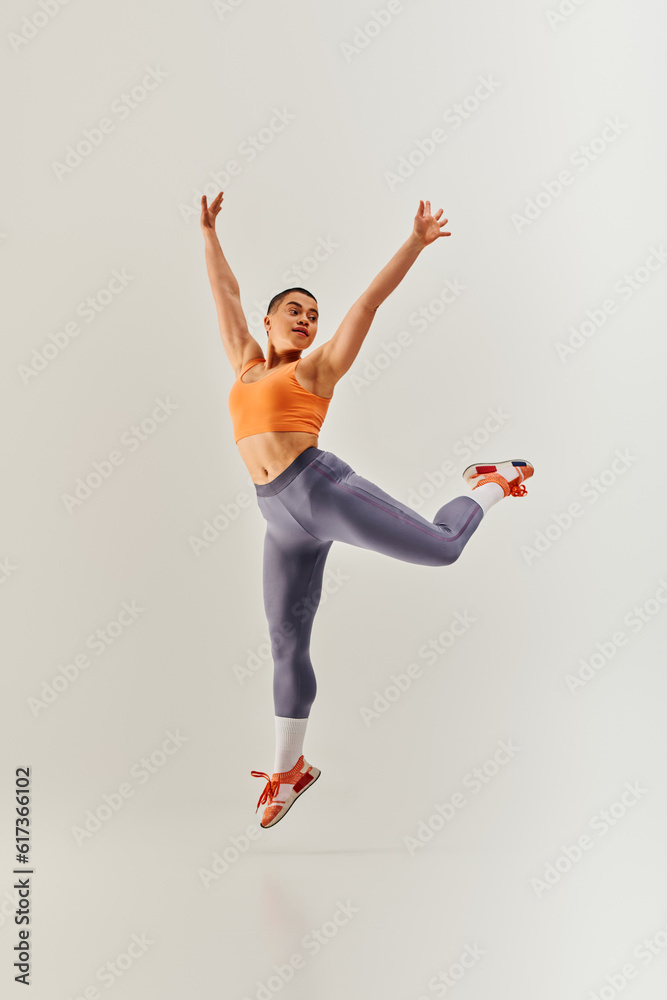body positivity movement, young curvy and short haired woman jumping on grey background, female fitness, empowerment, motivation, working out, sportswear, strength and health, body image