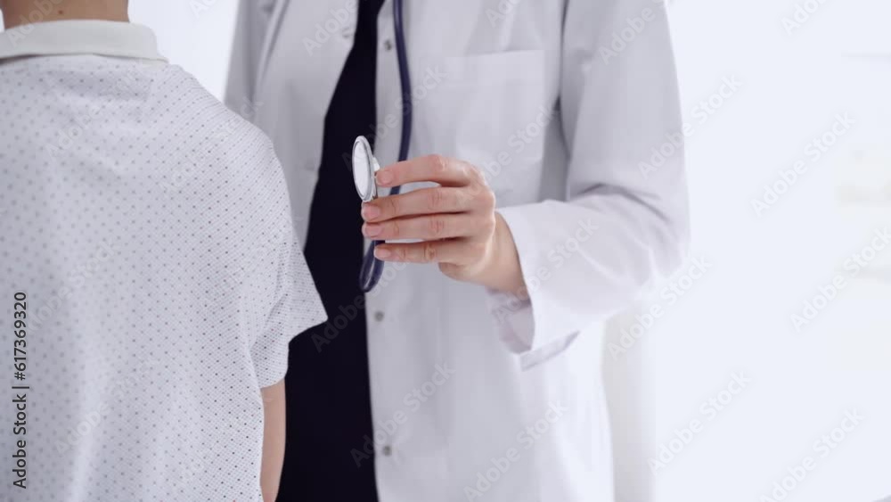 Doctor and kid patient are in the clinic. Physician in white coat examining a young boy's back with a stethoscope, close up. Medicine, therapy concept Doctor and kid patient are in the clinic. Physician in white coat examining a young boy's back with a stethoscope, close up. Medicine, therapy concept