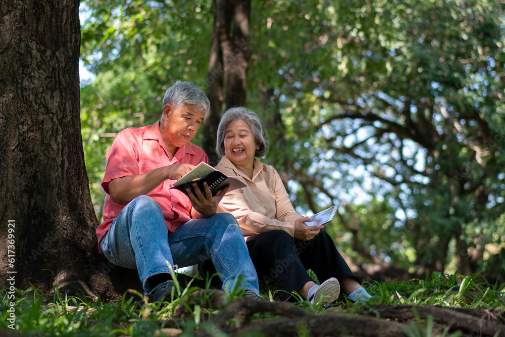 Happy Asian old senior couple with gray hair reading a book outside in park. Concept of happy elderly after retirement and good health Happy Asian old senior couple with gray hair reading a book outside in park. Concept of happy elderly after retirement and good health
