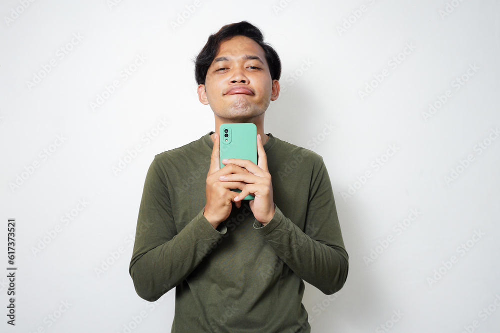 Adult Asian man looking to camera think something while typing on his mobile phone Adult Asian man looking to camera think something while typing on his mobile phone