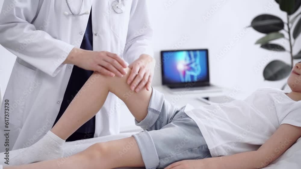Doctor and patient are in the clinic. Orthopedic in white coat examines knee joint of a kid girl, close up. Medicine, physical therapy concept