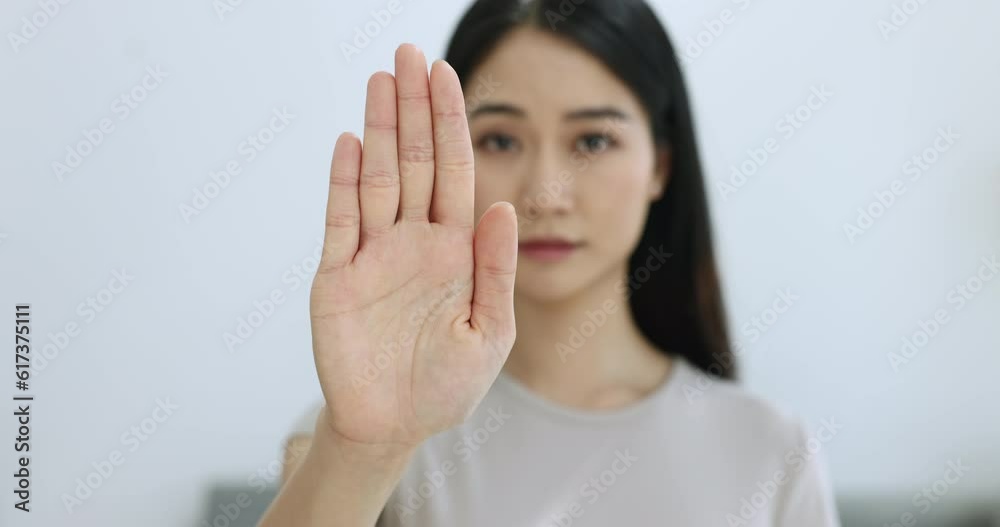Close up serious Asian woman show palm to camera demonstrate stop gesture, sign of anti domestic violence, racism racial discrimination, fight for women rights, pose indoor look with strict expression Close up serious Asian woman show palm to camera demonstrate stop gesture, sign of anti domestic violence, racism racial discrimination, fight for women rights, pose indoor look with strict expression