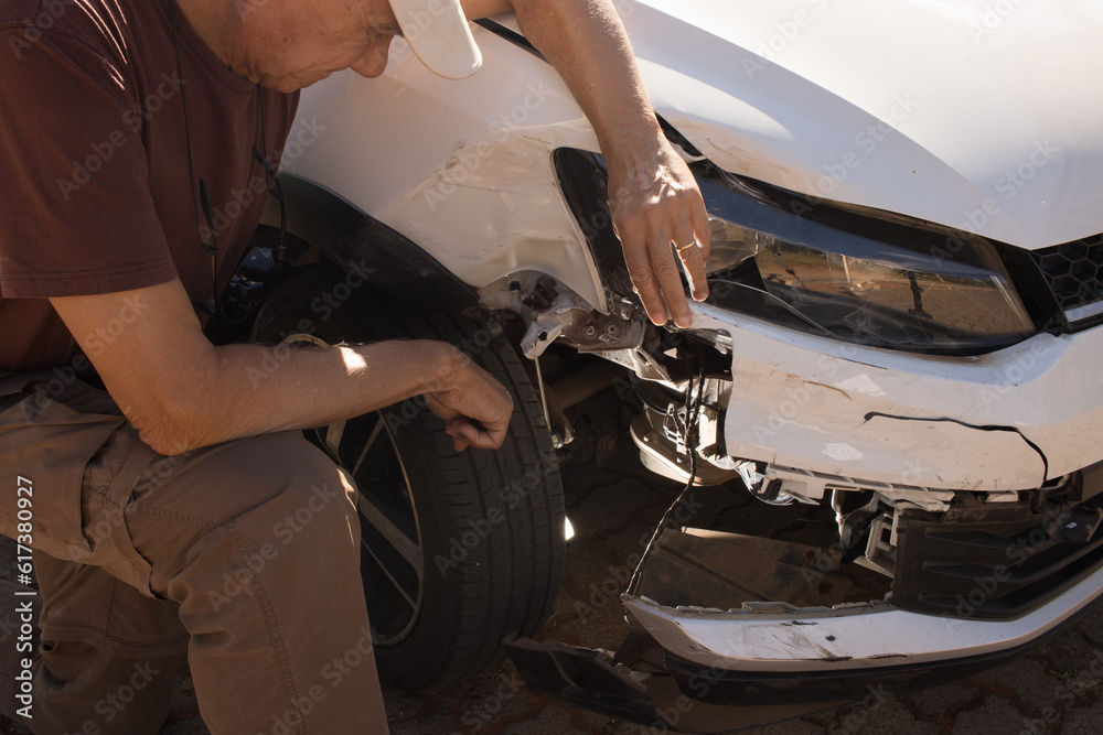 Man checking out the damage to the right front end of his car that was in a collision Man checking out the damage to the right front end of his car that was in a collision