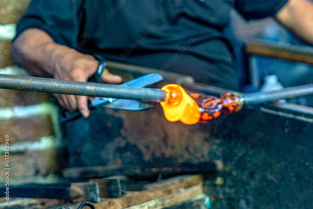 Old craftsman with scissors cutting and blowing the glass in fusing temperature to make a bottle with the old technique of blown glass, it is a very old and craft technique. Concept craftsmen. Old craftsman with scissors cutting and blowing the glass in fusing temperature to make a bottle with the old technique of blown glass, it is a very old and craft technique. Concept craftsmen.