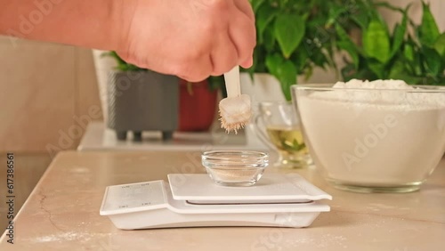 A woman measures dry yeast into a glass bowl standing on an electronic scale. Preparation of yeast dough for pizza.