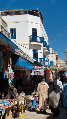 Alley lined with souvenir shops below white buildings with blue trim in the Medina in Essaouira, Morocco © Angela