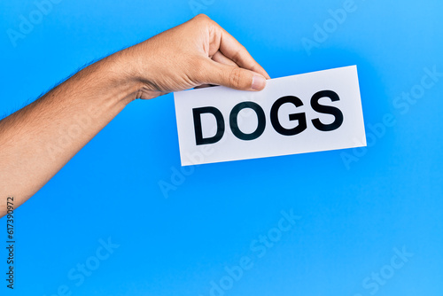 Hand of caucasian man holding paper with dogs word over isolated blue background