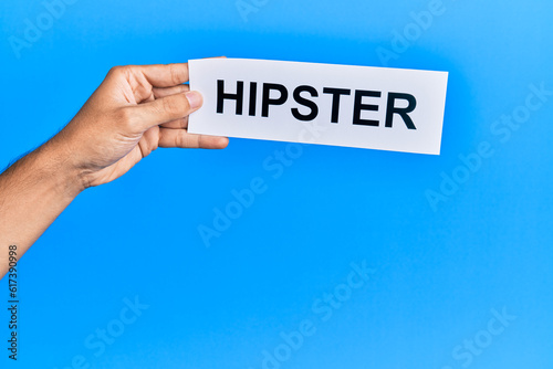 Hand of caucasian man holding paper with hipster word over isolated blue background