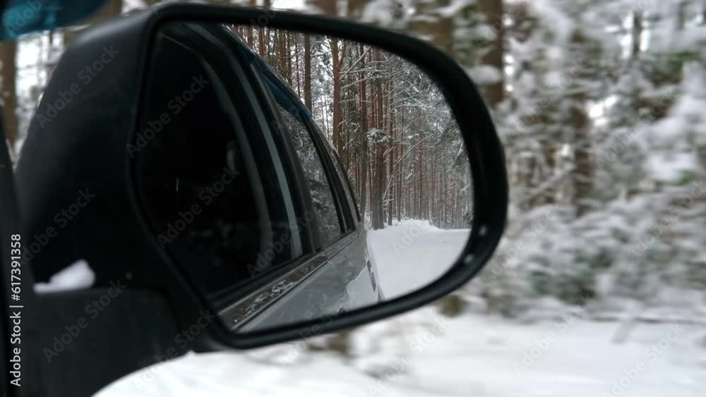 Side view mirror reflection of winter forest road. Landscape with empty highway going through the Snowy forest. Car speeding on road. Auto in motion. Tourism, travel, trip concept. Snow covered trees.