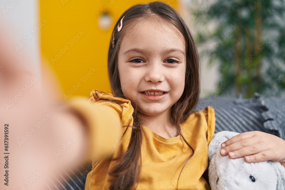 Adorable hispanic girl make selfie by camera sitting on sofa at home