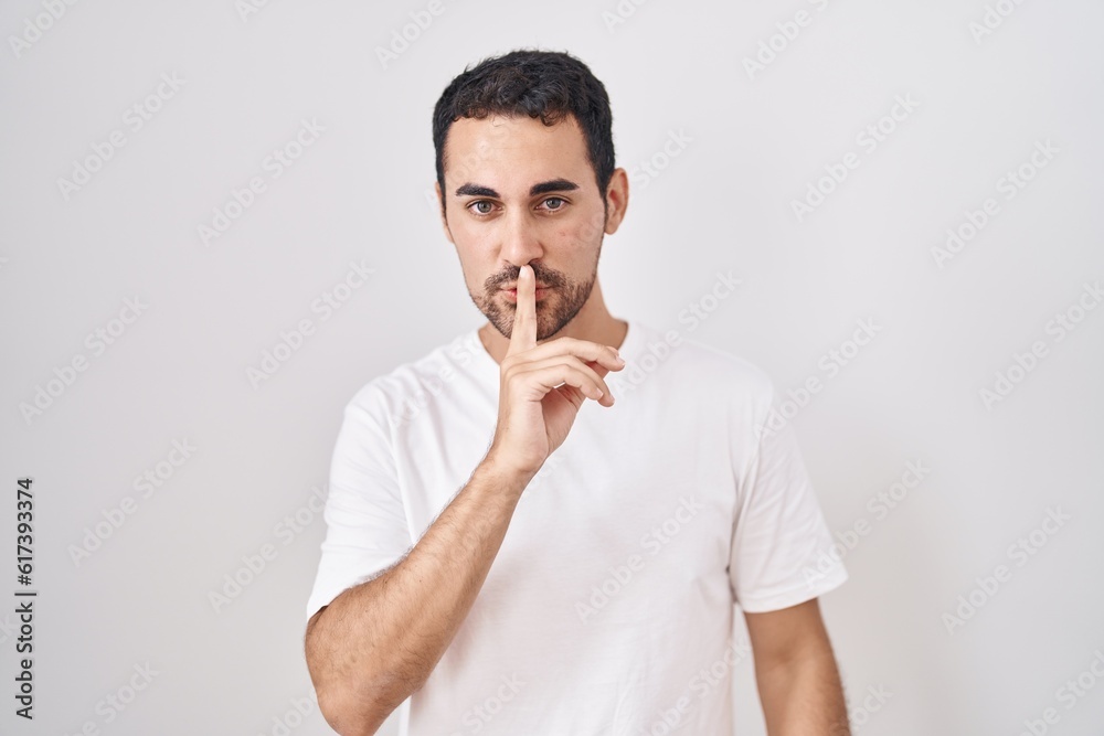 Handsome hispanic man standing over white background asking to be quiet with finger on lips. silence and secret concept. Handsome hispanic man standing over white background asking to be quiet with finger on lips. silence and secret concept.
