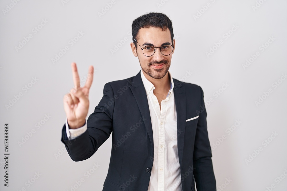 Handsome business hispanic man standing over white background showing and pointing up with fingers number two while smiling confident and happy. Handsome business hispanic man standing over white background showing and pointing up with fingers number two while smiling confident and happy.