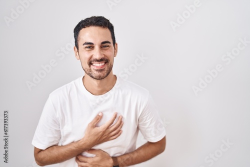 Handsome hispanic man standing over white background smiling and laughing hard out loud because funny crazy joke with hands on body.