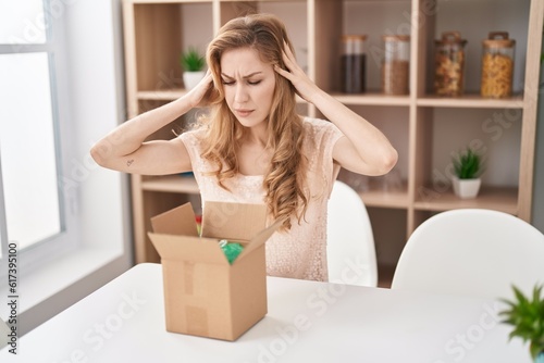 Beautiful blonde woman with cardboard box with hand on head, headache because stress. suffering migraine. © Krakenimages.com