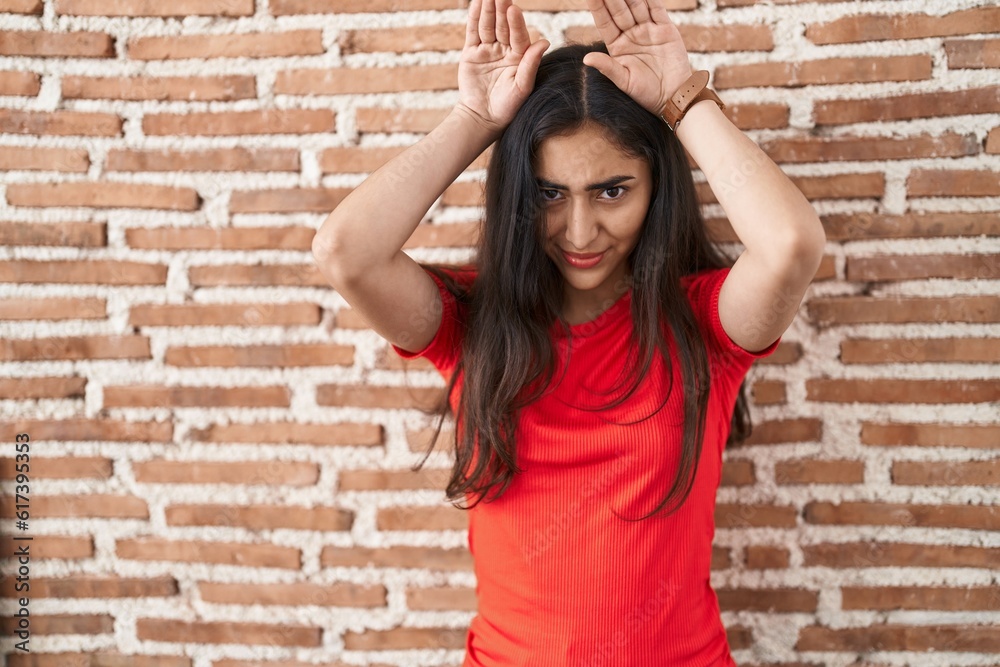Young teenager girl standing over bricks wall doing bunny ears gesture with hands palms looking cynical and skeptical. easter rabbit concept. Young teenager girl standing over bricks wall doing bunny ears gesture with hands palms looking cynical and skeptical. easter rabbit concept.