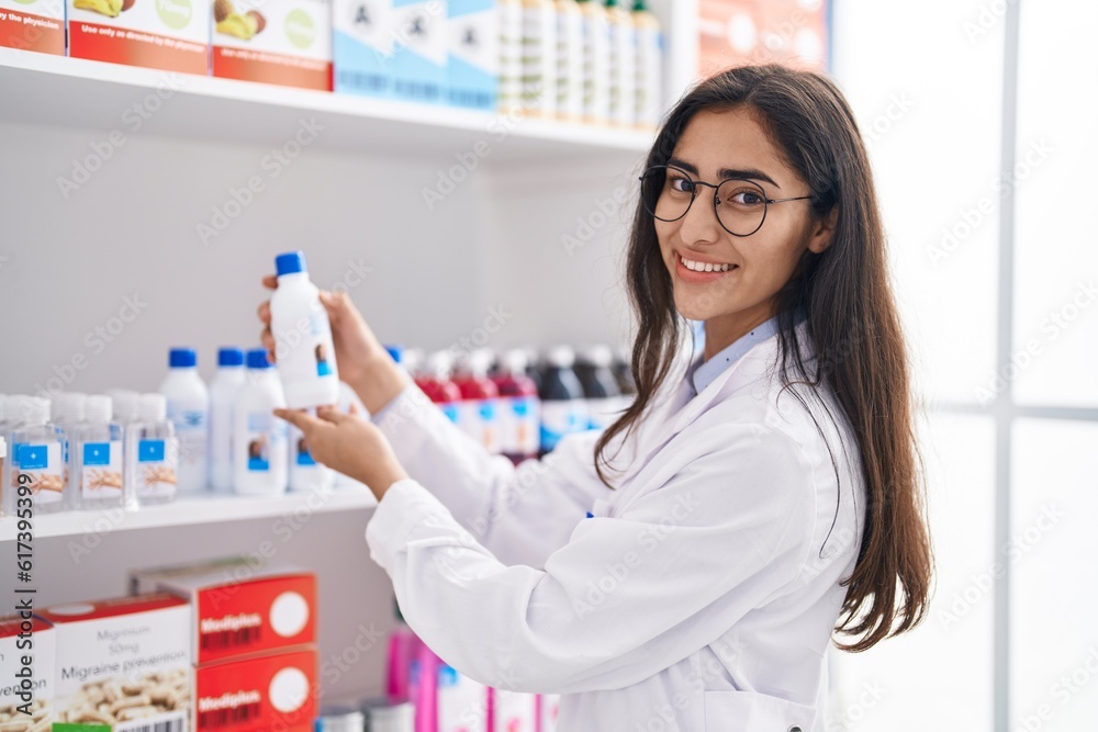Young hispanic girl pharmacist organizing shelving at pharmacy