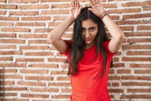 Young teenager girl standing over bricks wall doing bunny ears gesture with hands palms looking cynical and skeptical. easter rabbit concept.