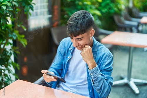Young hispanic man watching video on smartphone sitting on table at coffee shop terrace © Krakenimages.com