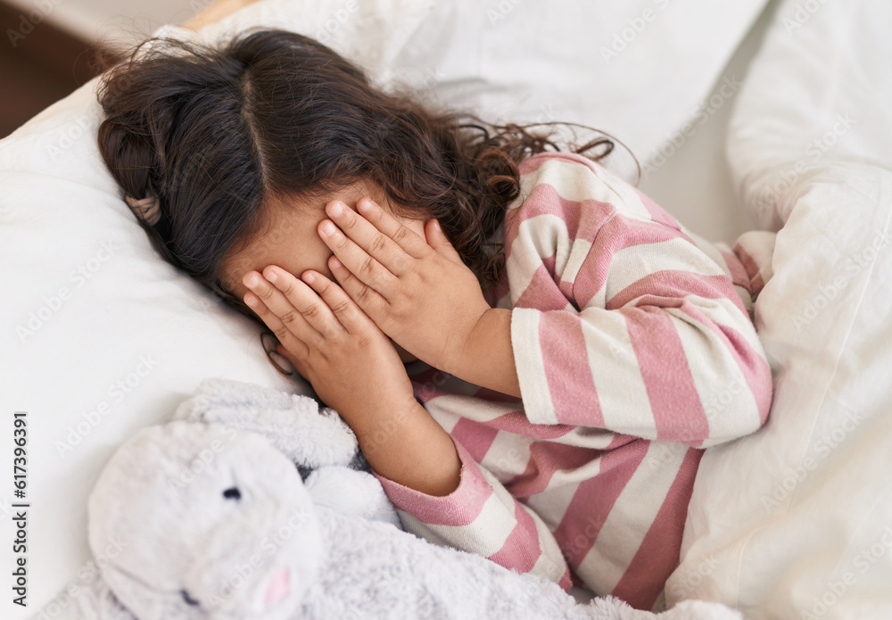 Adorable hispanic girl lying on bed covering eyes with hands at bedroom Adorable hispanic girl lying on bed covering eyes with hands at bedroom