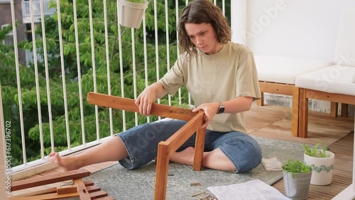 Confused  young curly woman trying to assemble new garden furniture on her balcony on her own.