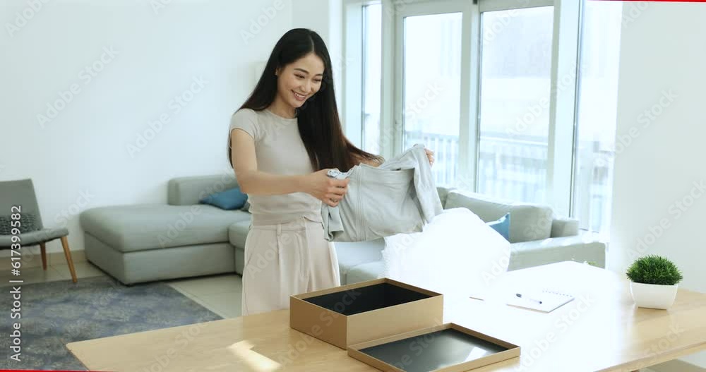 Young Asian woman, e-commerce online webstore retail services client, opens parcel box, unpack fashion clothes smiles enjoy express delivery e-services feel satisfied and quality and remote e-shopping Young Asian woman, e-commerce online webstore retail services client, opens parcel box, unpack fashion clothes smiles enjoy express delivery e-services feel satisfied and quality and remote e-shopping
