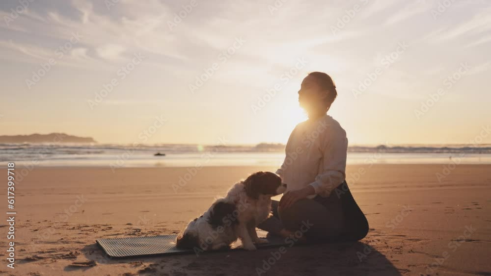 Woman meditating with dog on ocean beach at sunset. Female relaxing and doing mental exercises on Yoga mat on sand sea shore at sunrise. Strong powerful woman in the morning or evening outdoors. 