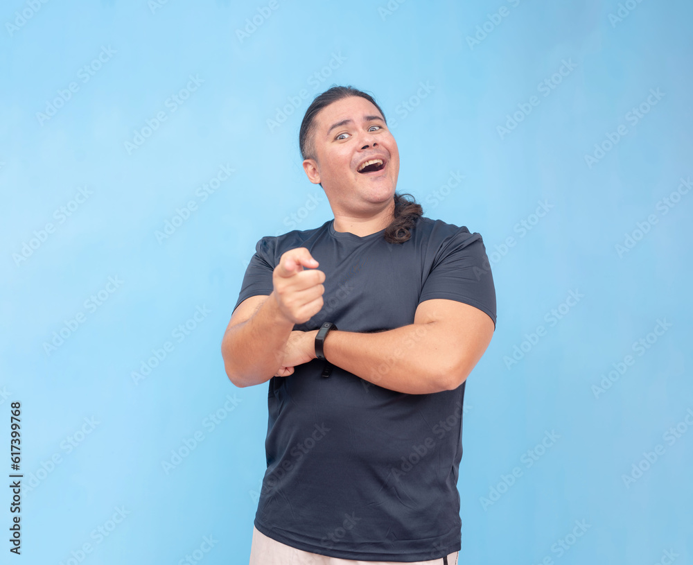 A skeptical and amused biracial male with head tilted up while chuckling, pointing forwards, and one arm across chest. Isolated on a blue background. A skeptical and amused biracial male with head tilted up while chuckling, pointing forwards, and one arm across chest. Isolated on a blue background.