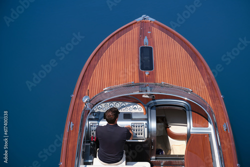 Fashion wooden boat with a man on the water aerial view. Luxury boat on the water. Luxurious big boat for millionaires deck part on blue water top view.