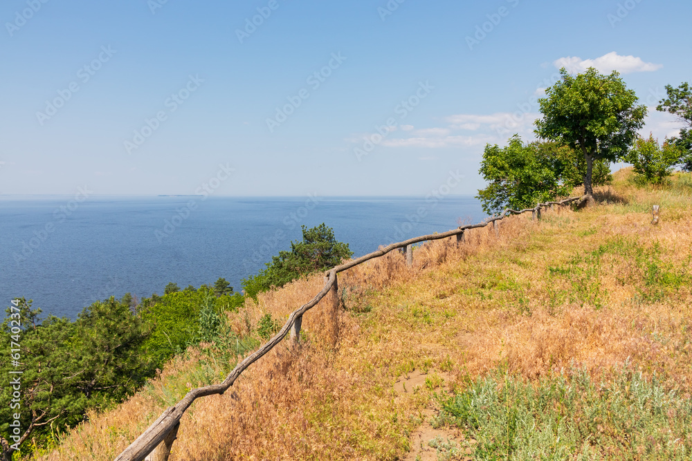Observation deck on a hill with wooden railings and views of the reservoir or the sea. Summer landscape with trees and grass