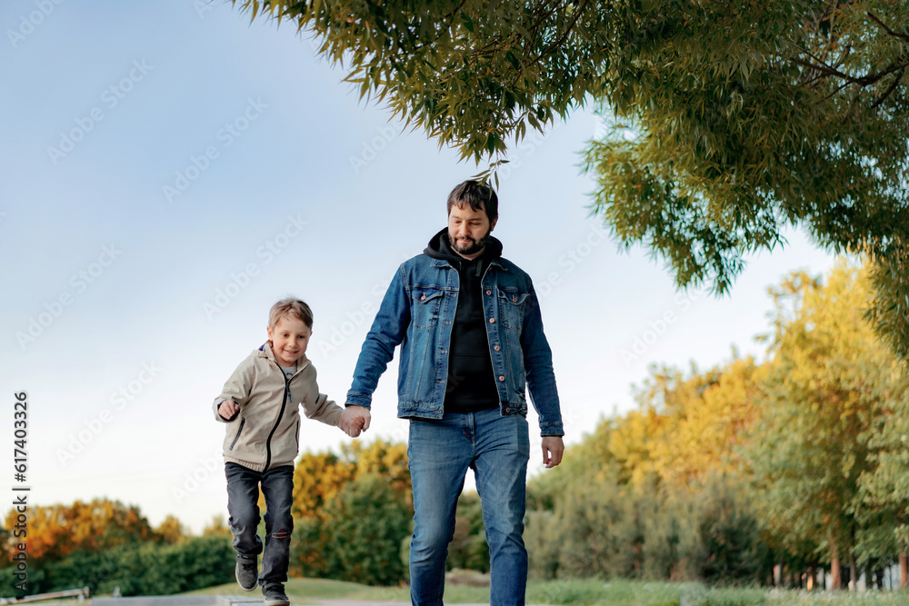 Caucasian bearded man with his little son walking in park holding hands on autumn day