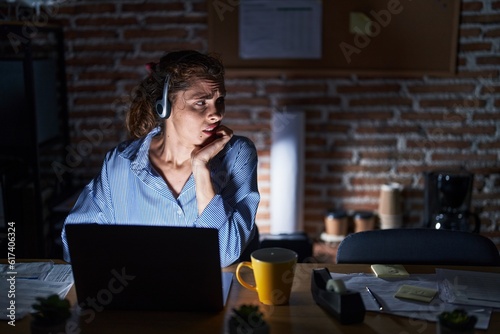 Beautiful brunette woman working at the office at night looking stressed and nervous with hands on mouth biting nails. anxiety problem.