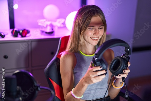 Young blonde woman streamer playing video game holding headphones at gaming room