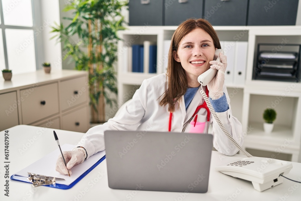 Young blonde woman doctor talking on telephone writing on document at clinic Young blonde woman doctor talking on telephone writing on document at clinic